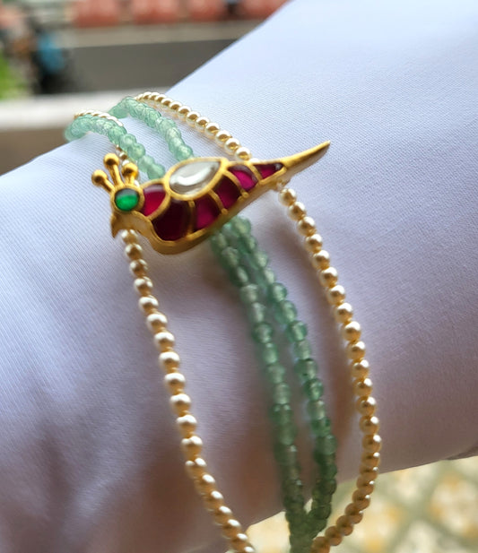 Close-up of a wrist wearing multiple beaded bracelets with a decorative gold and red gemstone clasp.
